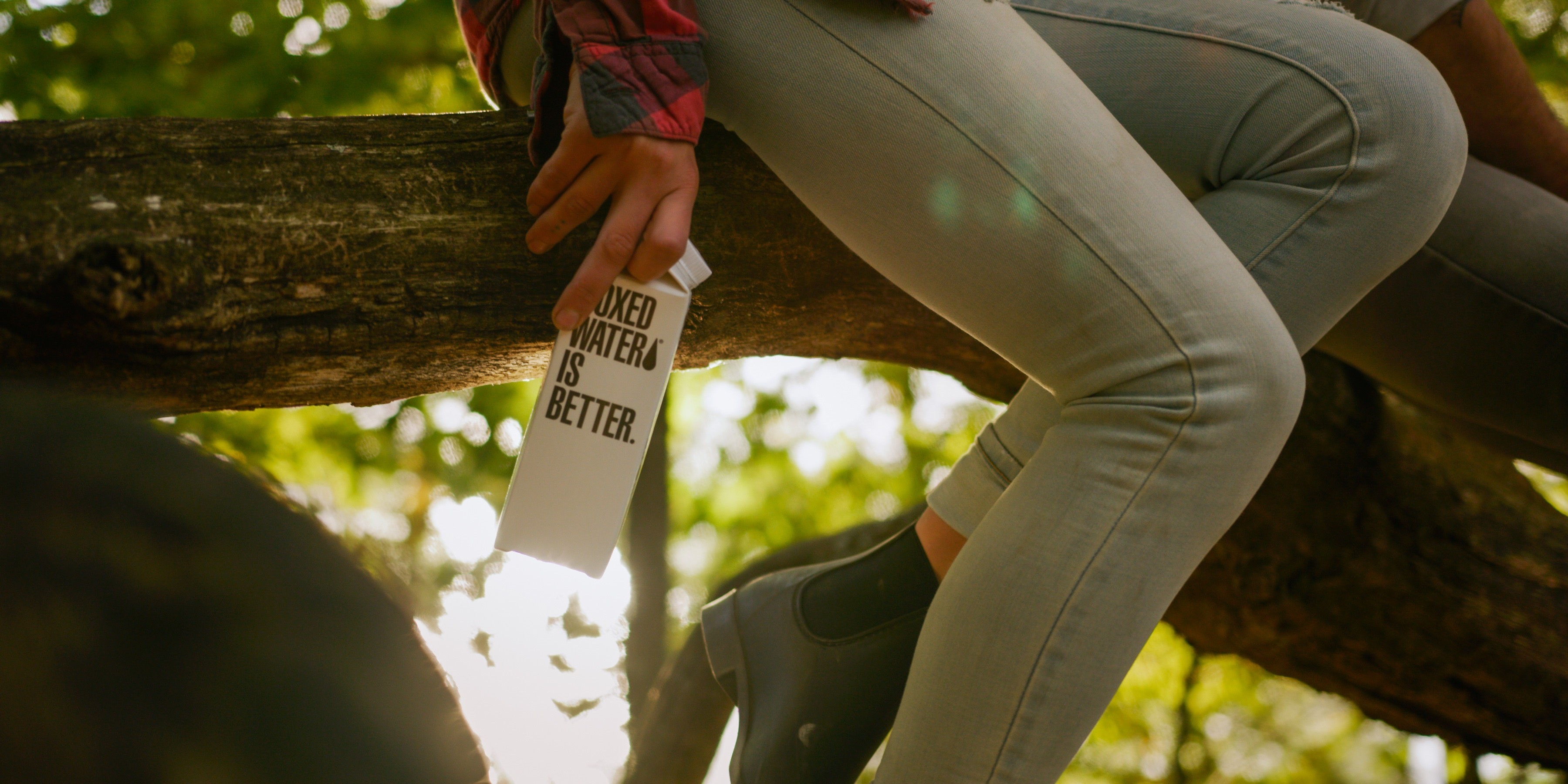 Hand holding a plant, person in nature wearing pants and shoe, 1D barcode, text: JXED WATER IS BETTER.