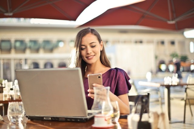Person sitting at table with laptop, smiling while wearing clothing, using personal computer.
