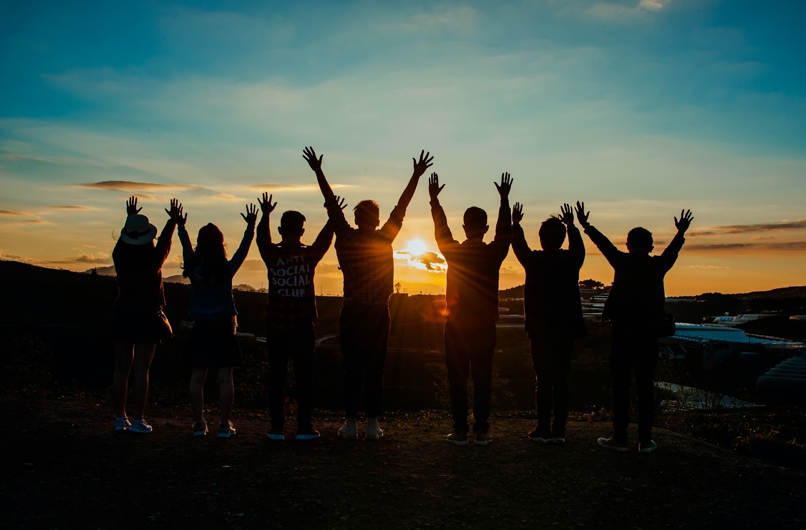 Cloudy sky overlooking three individuals in nature, with one person making a gesture wearing clothing that spells out "ANTI SOCIAL SOCIAL CLUB".