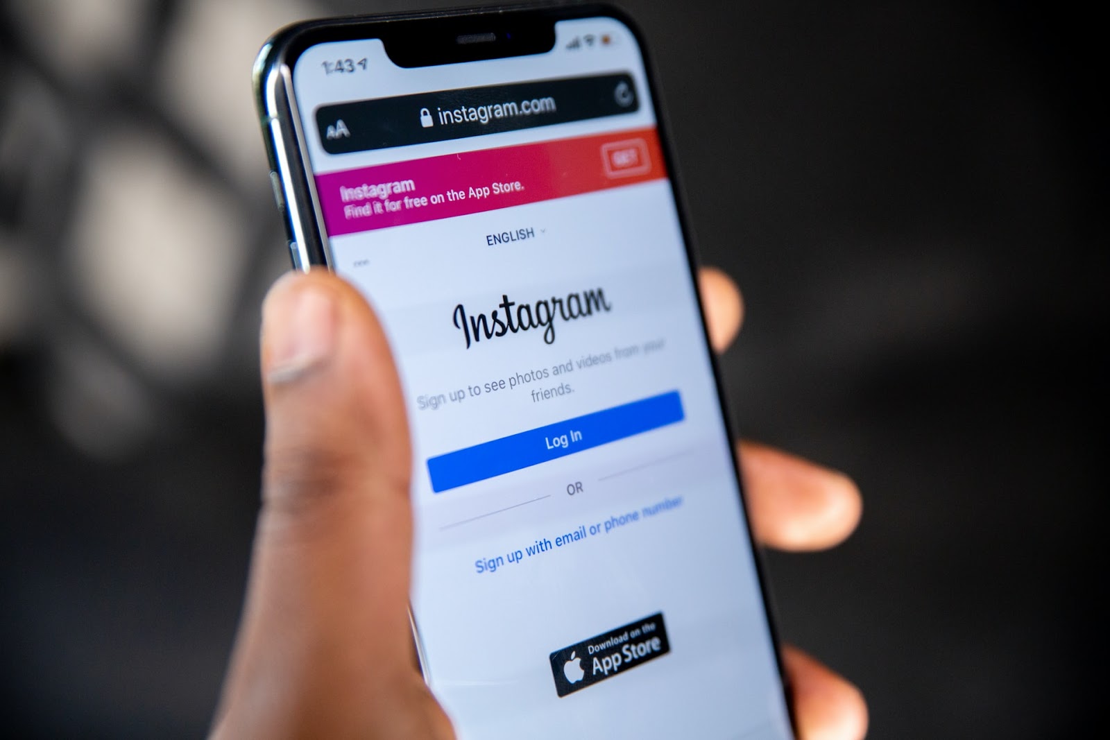 Mobile phone displaying the Instagram app landing page with options to sign up, log in, and download from the App Store.