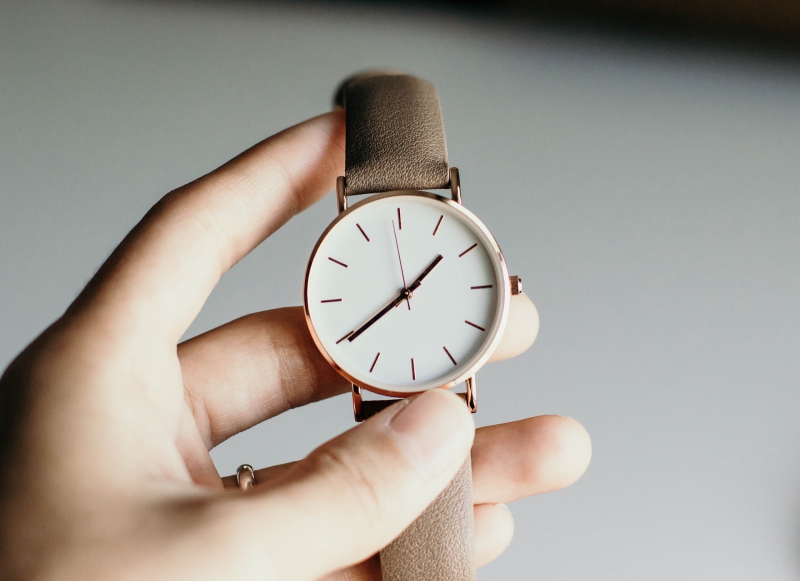 Hand holding an analog watch showing a specific time with a gesture, emphasizing the importance of time management.