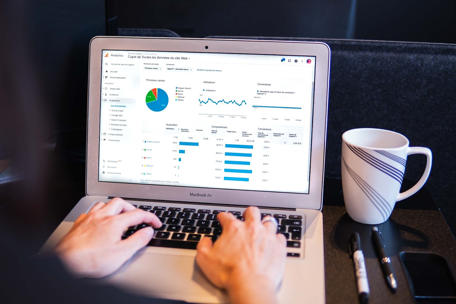 Computer screen showing various website analytics data with sections labeled in French, text in a different language, and a MacBook Air in the background.