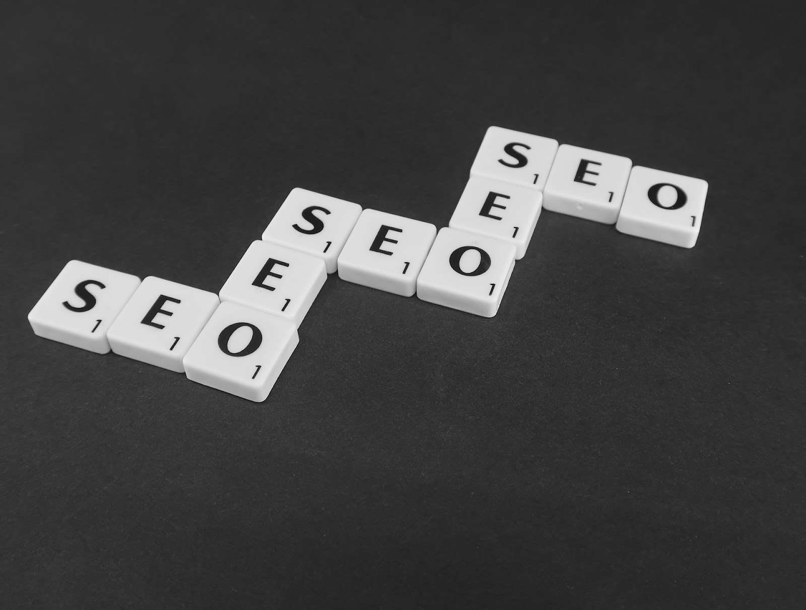 SEO text on a wooden rectangle with symbols S, E, O arranged in a grid pattern.