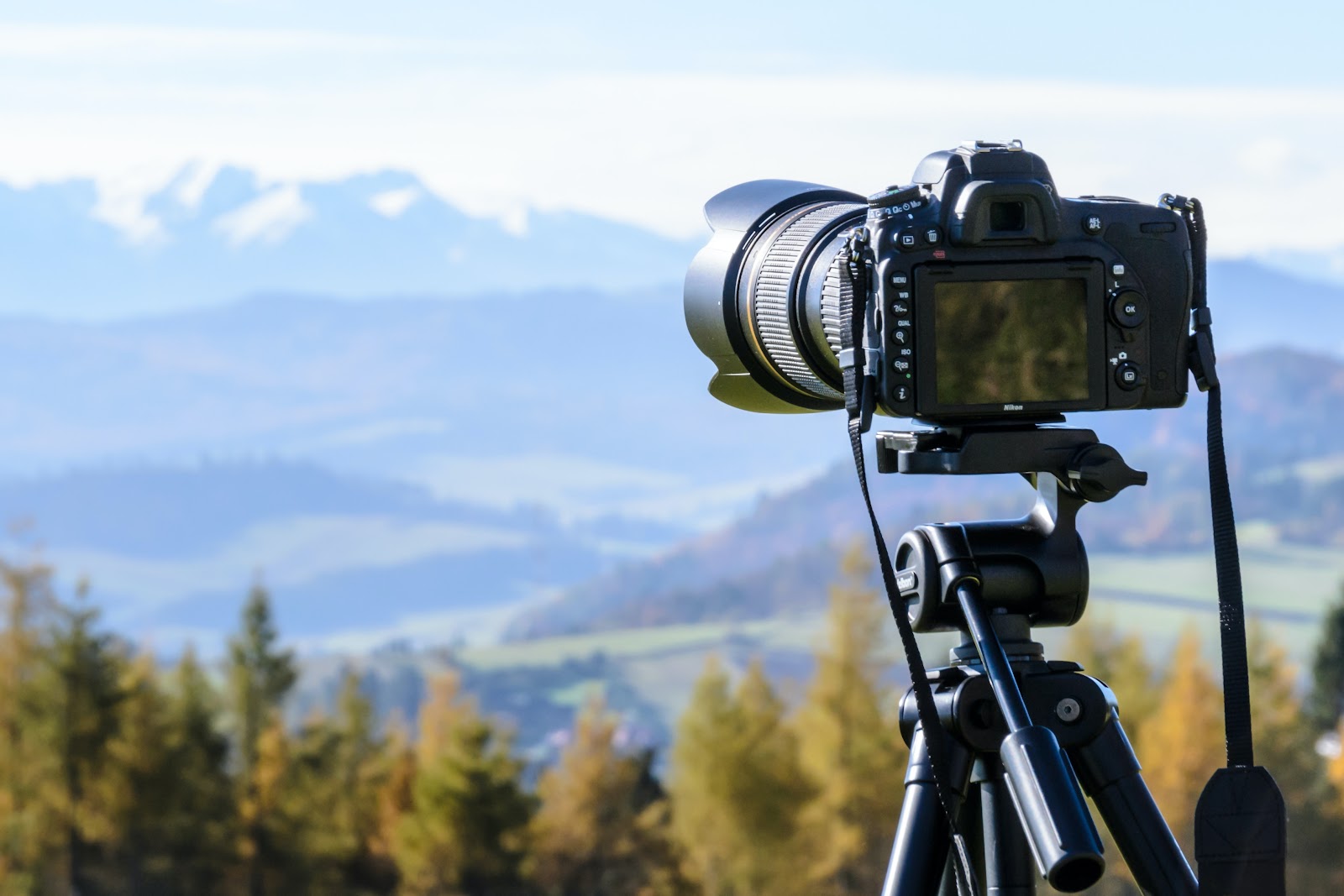 Sky with fluffy white clouds, camera lens, single-lens reflex camera on a tripod, accompanied by camera accessories, against a backdrop of light blue sky.