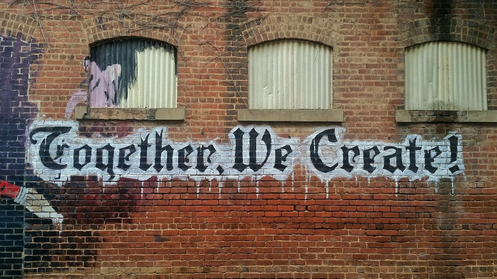 Brown brick building with multiple windows and window blinds, with text "Together We Create!"
