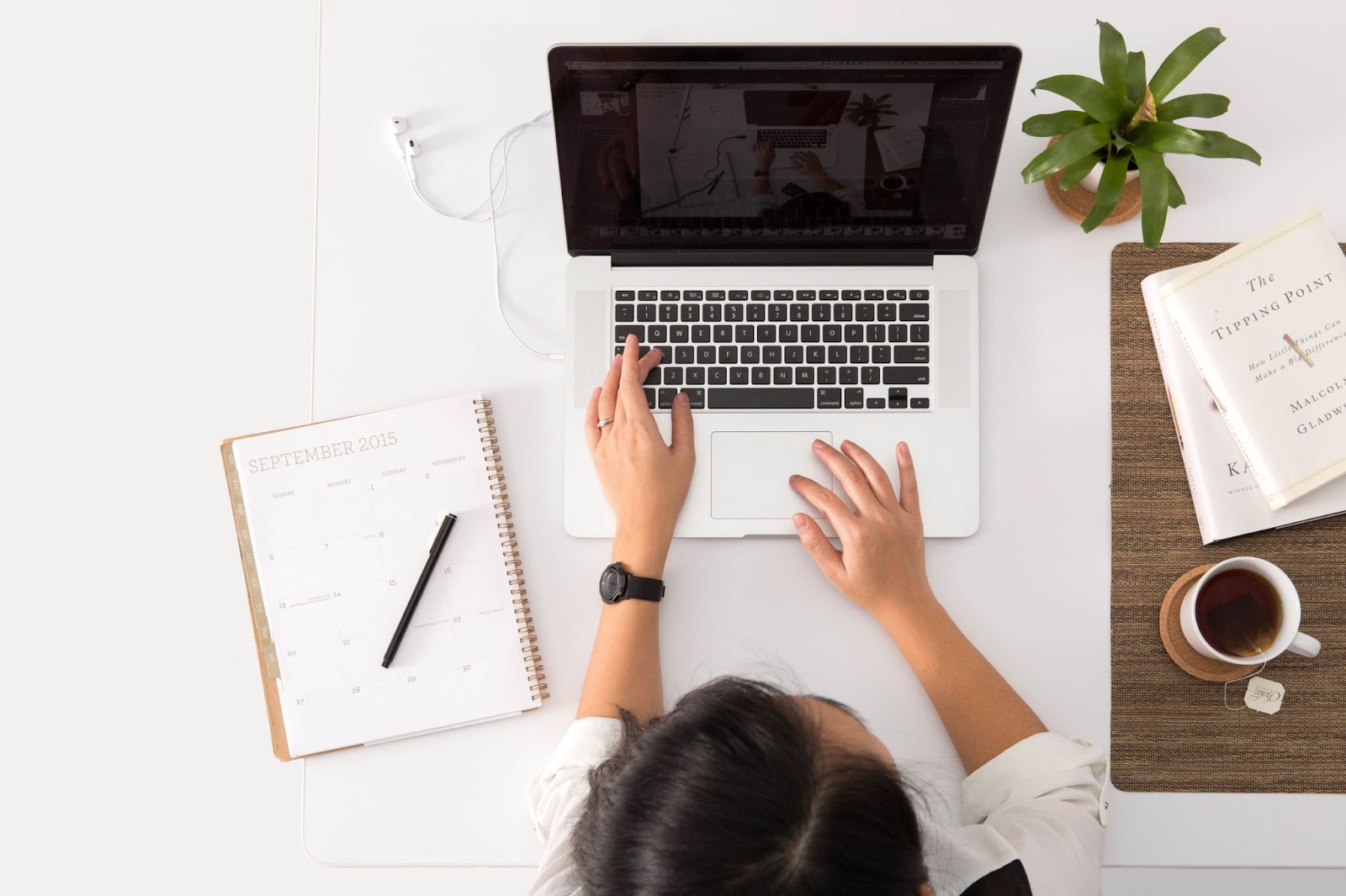 Watch, person using laptop to work on a computer keyboard, notebook with text "SEPTEMBER 2015", calendar dates, book title "The Tipping Point"