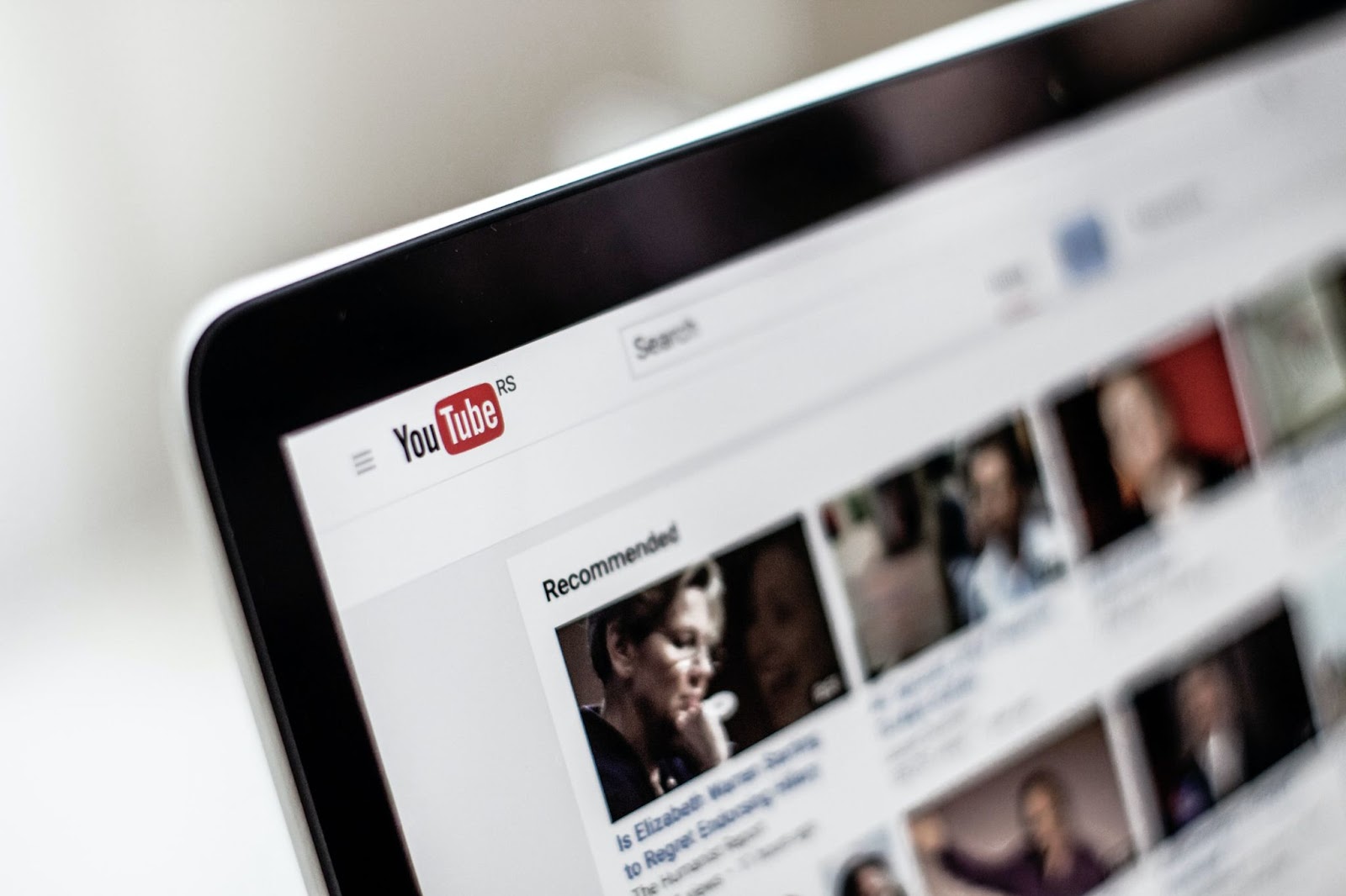 Computer with text "YouTube," "RS Search," "Recommended," "Is Elizabeth Wa," and "to Regret Ends" displayed on screen, person making a gesture, communication device.