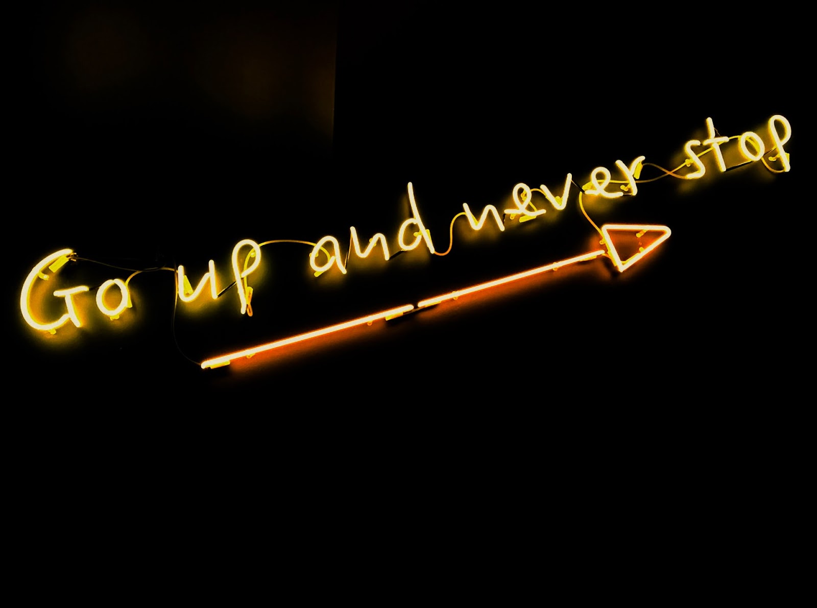 Amber electronic sign at a marketing event displaying the message "Go up and never stop" in a bold font on a rectangular screen.