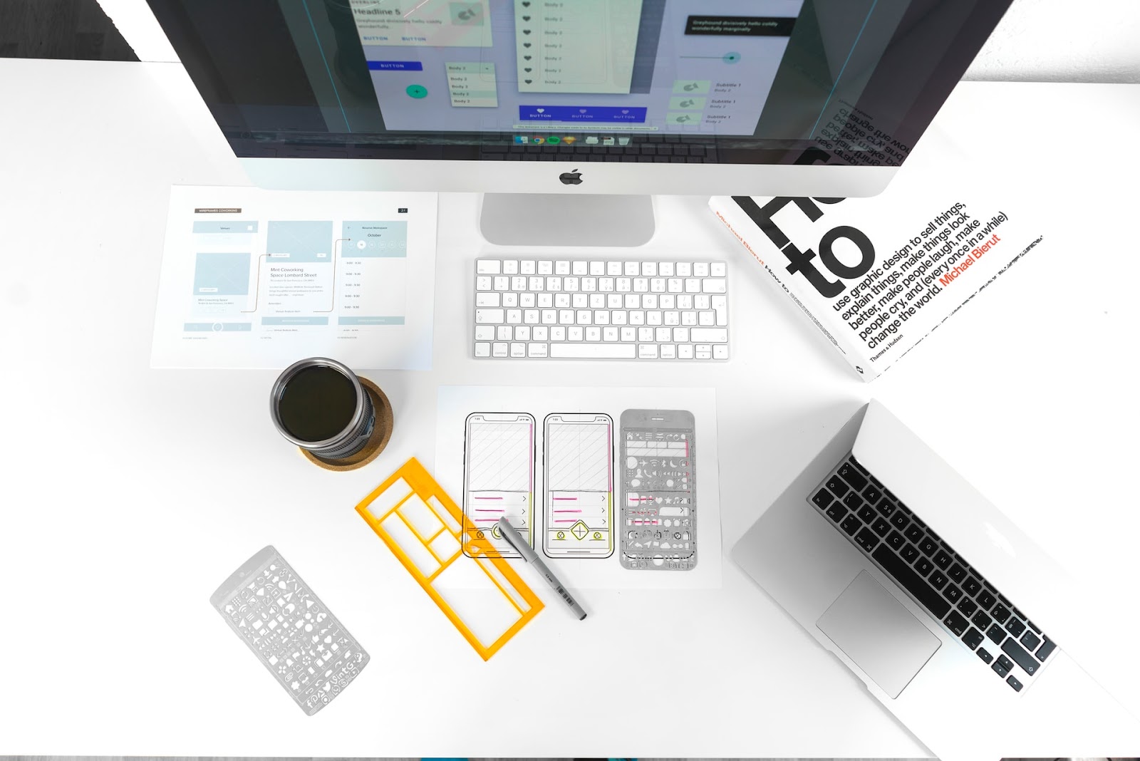 Computer setup with keyboard, monitor, and a drink on a table, accompanied by a book titled "How to Use Graphic Design".