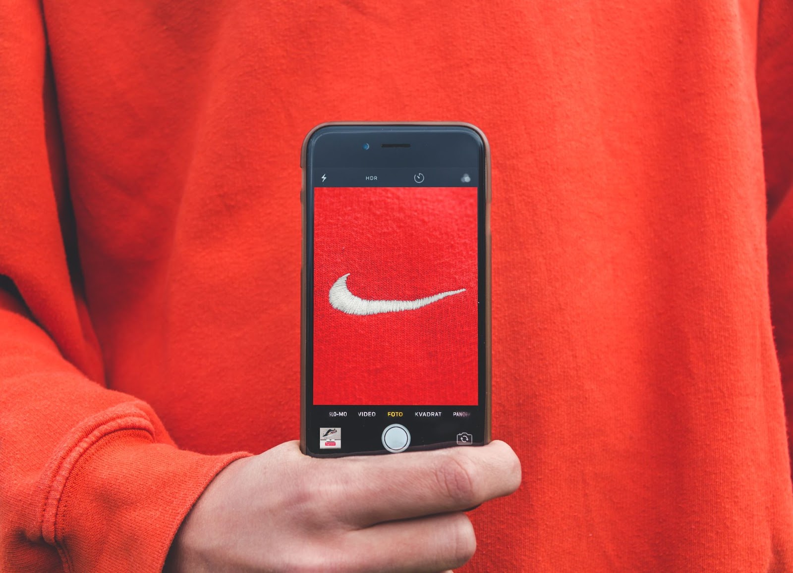 Outerwear product with jersey sleeve featured next to a communication device and mobile phone displaying text "SLO-MO VIDEO FOTO KVADRAT PANOR 3 HDR."