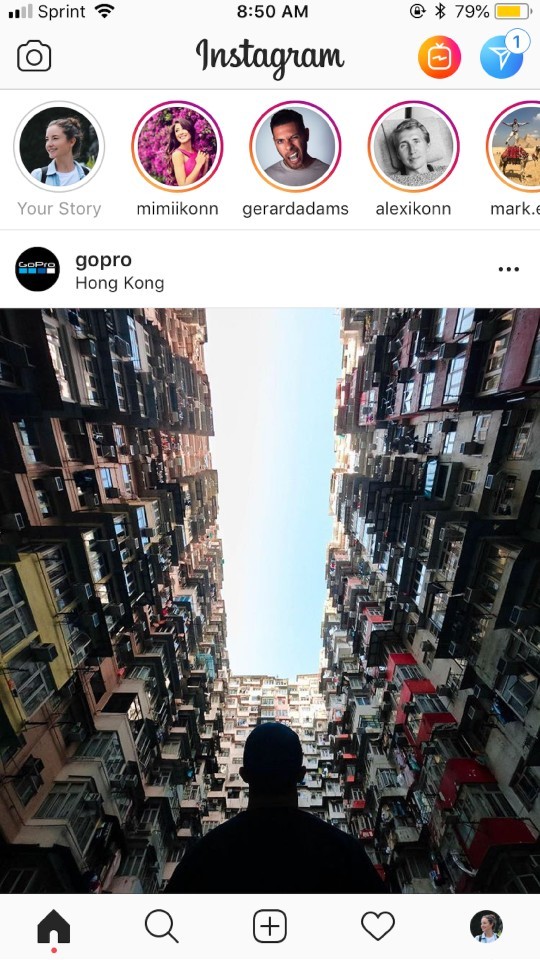Photograph of four people in front of a lighted world building in Hong Kong, holding a gopro, with Instagram stories displayed on a phone screen.