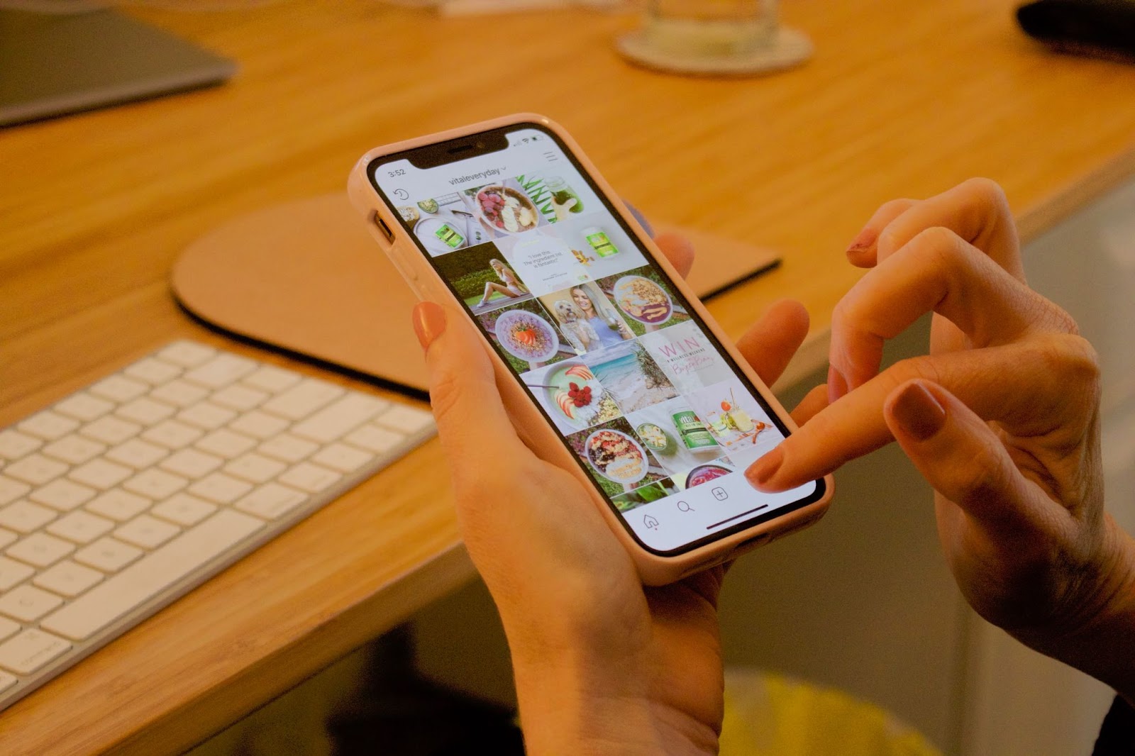 Hand holding an orange mobile phone with a computer keyboard in the background, displaying the text "NIM ANN vitaleveryday"