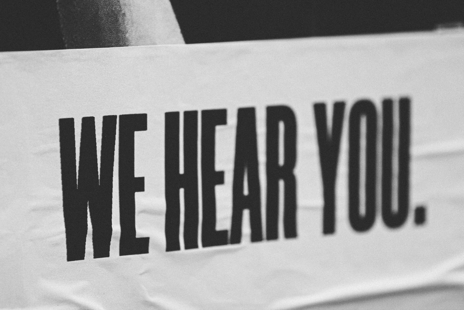 Black sleeve with "WE HEAR YOU" text in a trendy font on a rectangular wooden background.