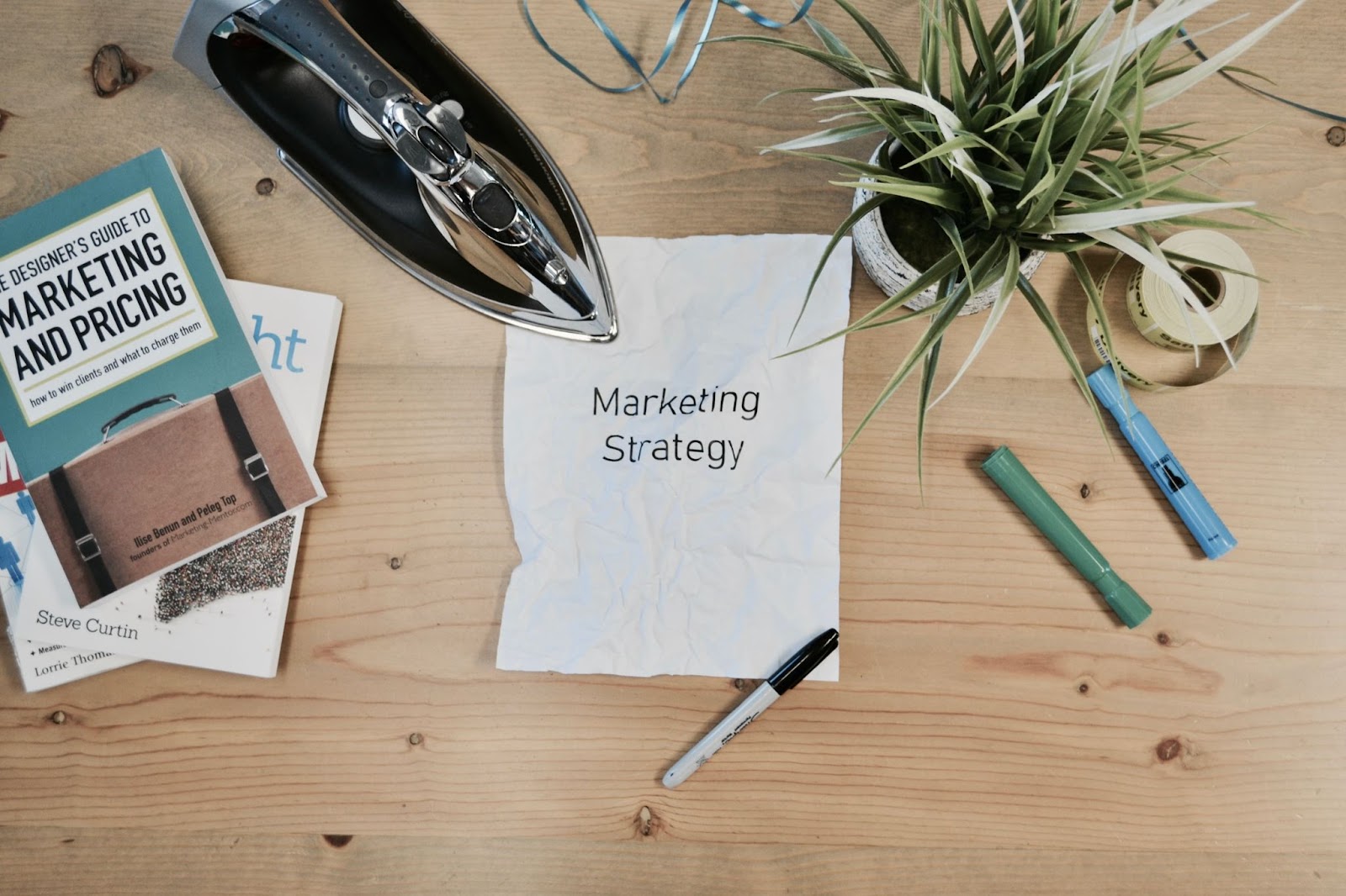 Table with plant, wood, office supplies, and a book cover "The Designer's Guide to Marketing and Pricing" by Steve Curtin, Lorrie Thom, Ilise Benun, and Peleg Top.