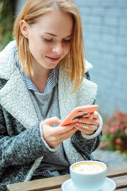 A person holding a coffee cup and mobile phone, with tableware and drinkware in the background.